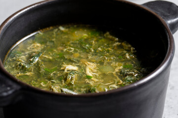 Soup with green sorrel in black ceramic pot on gray background