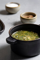 Soup with green sorrel in black ceramic pot on gray background
