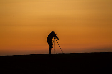 In this striking silhouette, a photographer stands poised against a breathtaking backdrop, capturing the essence of a moment. The outline of their figure, framed by the soft glow of the setting sun.