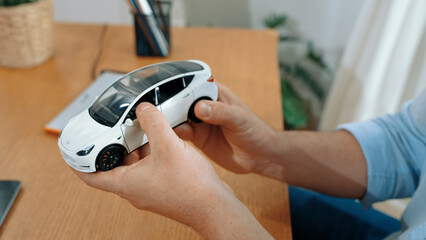 Car design engineer analyze car model prototype for automotive business company at home office. Vehicle designer holding scale car, carefully analyzing looking for any flaw or improvement. Synchronos