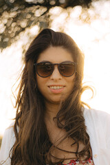 Beautiful young woman looks at the camera. Portrait of an attractive brunette with long hair. A tanned girl in sunglasses smiles at the camera. Grain photo