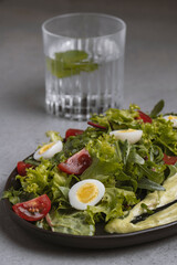 Fresh green salad with quail eggs, cherry tomatoes and guacamole in black plate on grey background