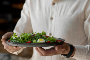 Close-up of a man holding a bowl of salad with eggs and cherry tomatoes. Waiter