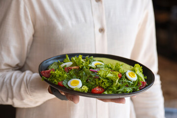 Close-up of a man holding a bowl of salad with eggs and cherry tomatoes. Waiter