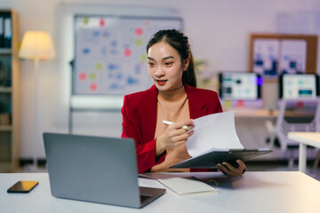 Young businesswoman is leading an online meeting while holding a pen and documents. She is sitting at her desk in a modern office