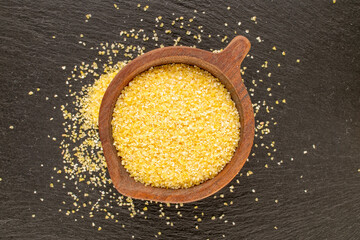 Uncooked corn grits with wooden cup on slate stone, macro, top view.