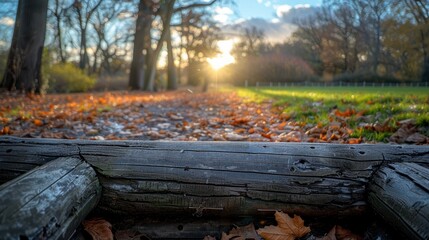 A serene autumn park scene captured during golden hour, featuring a trail covered with fallen leaves, wooden rails, and a breathtaking sunset in the background