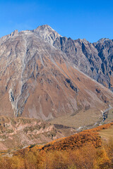 a panoramic view of autumn landscape with mountain hills surrounded by trees with yellow and red foliage at kazbegi stepantsminda in georgia near the foot of mount kazbek