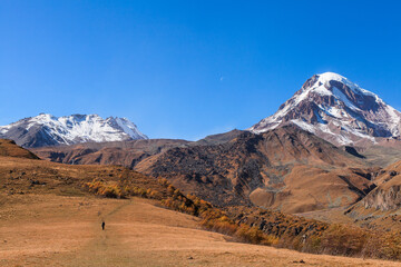 a panoramic view of autumn landscape with mountain hills surrounded by trees with yellow and red foliage at kazbegi stepantsminda in georgia near the foot of mount kazbek