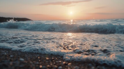 Waves gently lap against a pebble-strewn beach as the sun sets, casting warm hues over the calming ocean scene.