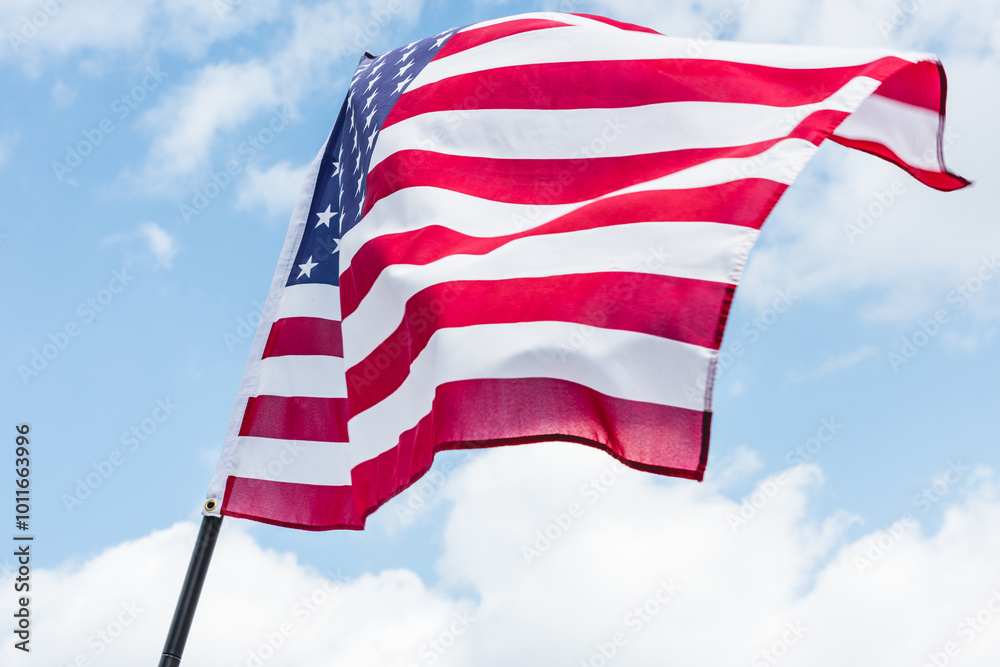 Sticker The American flag proudly flutters in the gentle breeze under a bright blue sky, celebrating patriotism.