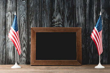 A pair of American flags standing proudly beside a blank wooden frame, symbolizing honor on...