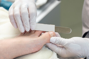 A pedicure technician files a client's toenails with a pedicure file