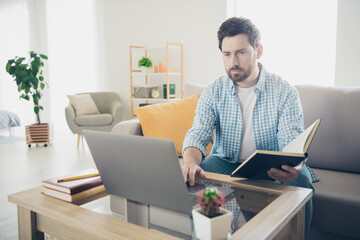 Photo of handsome bearded alone mature age adult man staying home in his new house indoors living room learning from book how use ai technology