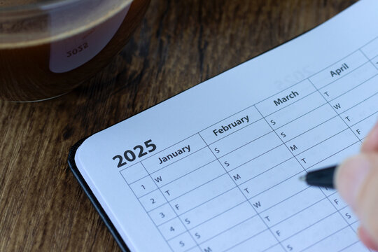 January 2025 year calendar, goal planner notebook with coffee cup on wooden desk. Monthly date organizer, schedule template. Close-up.