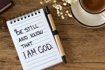 Be still and know that I am God, handwritten quote in notebook with coffee cup and holy bible. Top view. Christian biblical concept of waiting on Jesus Christ, patience, trust, protection, and peace.