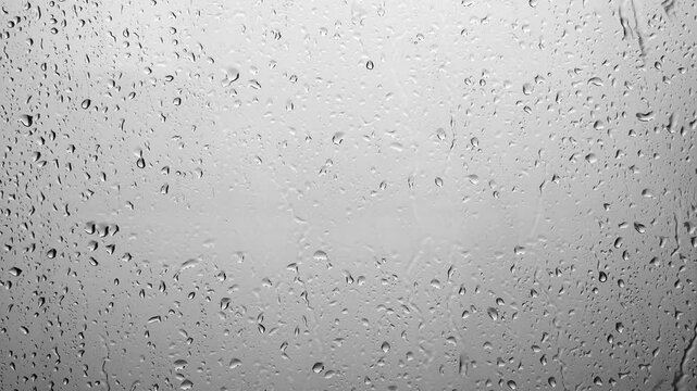 Raindrops falling down the window glass. Abstract background of raindrops in gray tones