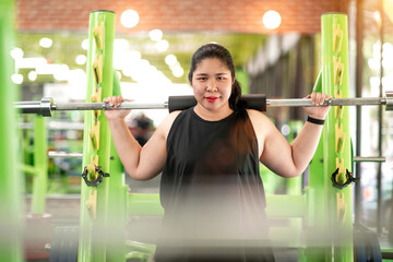 fat motivated woman exercise lifting barbell. determined chubby exerciser train body pushing heavy bar. female fat fitness gym member trying to practice lifting barbell exercise to reach healthy goal