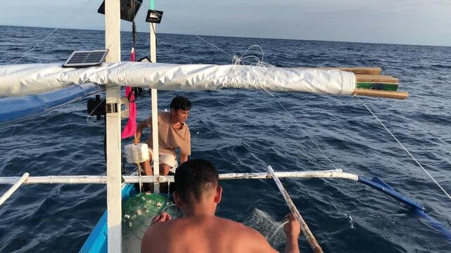 Fishermen are deploying a mile-long nylon fishing net in the sea from a wooden boat.