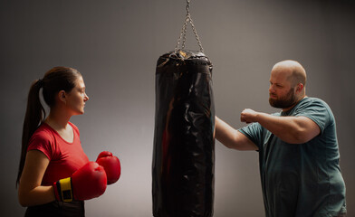 A strict trainer watches his teenager female kickboxer student practice a punch on a punching bag