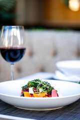 Gourmet beet salad with roasted beets, greens, nuts, cheese, elegantly plated in a modern dining setting. A pink cocktail and another dish blur in the background, enhancing the fine dining ambiance
