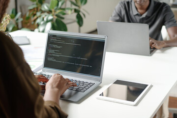 Medium close up of unrecognizable female worker sitting at work desk and writing code in modern office