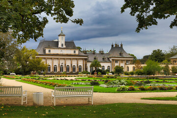 Obraz premium Blick über weiße Parkbänke im Lustgarten auf das barocke Bergpalais von Schloss Pillnitz unter einem dramatischen Wolkenhimmel in der Morgenstimmung, Dresden, Sachsen, Deutschland