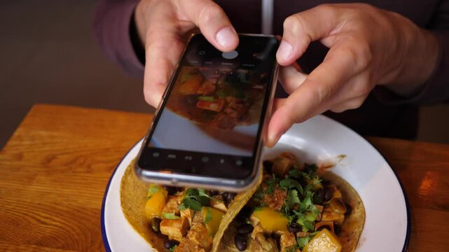 Food photo - man taking smartphone picture of tacos plate in Mexican restaurant for social media page