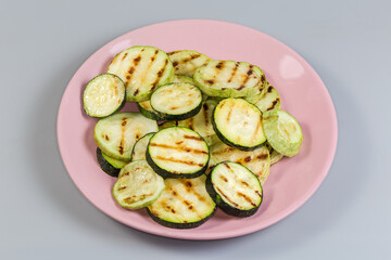 Grilled circles of zucchini and vegetable marrows on pink dish