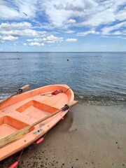 A small orange rescue boat docked on the shore of a beach with calm waters, under a partly cloudy...