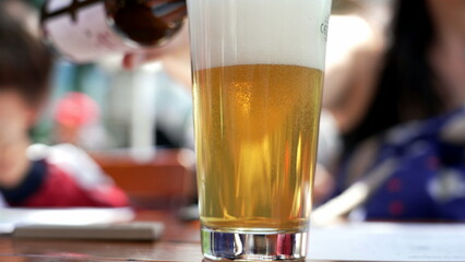 Close-up of beer being poured into a glass at an outdoor cafe, with a blurred background of a social setting, highlighting the refreshing nature of enjoying a cold drink