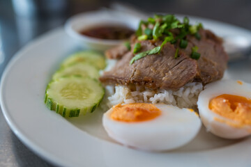 Slice of stewed pork eaten with rice served with boiled egg and cucumber sprinkled with coriander. Close up