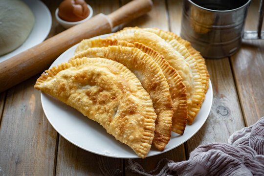 Hearty lunch: Chebureks with meat on a white plate on a wooden table. Big chebureks for dinner. Meat pies. Close-up.