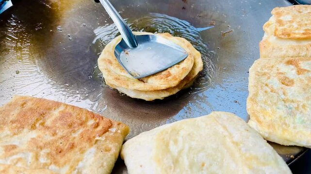 4k Street food vendor is preparing the dough and pan-frying paratha roti in hot oil until crispy on the outside. Street hawker preparing prata bread or roti canai for morning breakfast