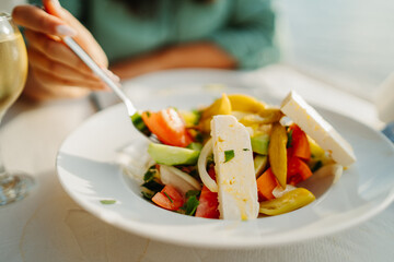 Young caucasian woman eating greek salad and drinking wine by the sea