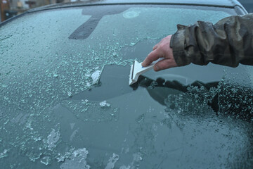 En hiver, une main racle un pare-brise de voiture avec un grattoir en plastique pour enlever le gel...