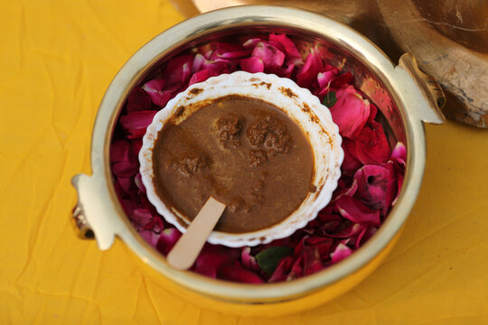 a bowl of natural, aromatic paste placed in a golden container lined with rose petals, offering a traditional, earthy aesthetic and a soothing ambiance.