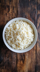 Overflowing white bowl filled with a generous serving of cooked white rice on a dark wooden table
