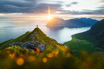 Midnight sun in Lofoten Islands. Breathtaking image of a young woman standing at the edge of a high...