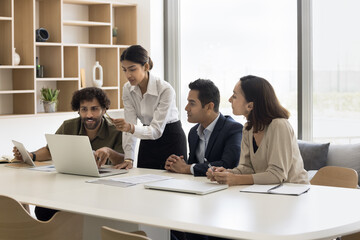 Young Indian woman executive coach explain project details to diverse interns on laptop....