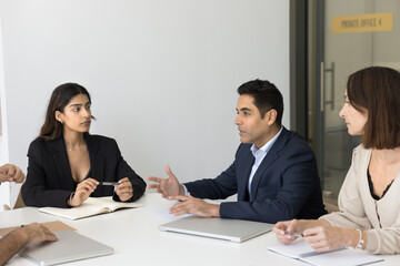 Inspired Indian man corporate worker speak share business plan to colleagues offer sales strategy express idea. Diverse shareholders investors group listen to report of expert on briefing in boardroom