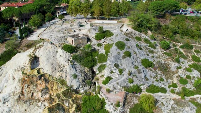 Bagno Vignoni&rsquo;s natural beauty captured with a winding path through rocky terrain and greenery, offering a peaceful escape into nature under a bright blue sky