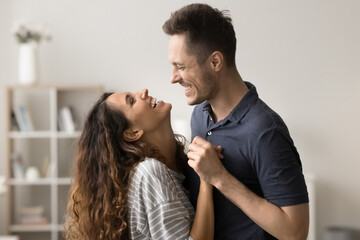 Joyful young couple in love hugging and dancing at home, talking, holding hands, laughing, enjoying romantic leisure time, activity, entertainment together, discussing good news
