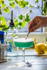 Bartender garnishing a blue cocktail with edible flowers and lemon zest