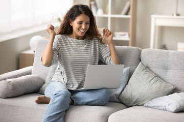 Cheerful young freelancer woman celebrating online business success, win at laptop, making yes hands, smiling, laughing, getting happy, excited, enjoying Internet connection technology