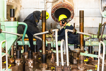 Two engine crew members are working together to replace an exhaust valve on the ship's main engine....