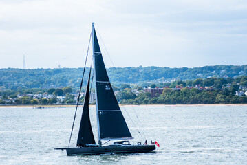 Naklejka premium A tourist yacht sails under full sails across the calm Atlantic waters near the coast of the USA, close to New York. The water shimmers silver, reflecting sunlight piercing through thick clouds.