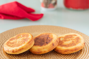 Three arepas boyacenses freshly prepared on a textured plate, in the background some out of focus elements stand out. Table served for breakfast. Concept of typical Colombian food.