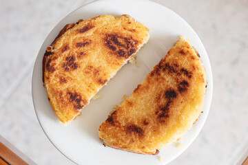 Top view of a grilled cheese arepa with golden brown edges and crunchy texture served on a white plate, cut in half and ready to eat. Traditional Colombian food concept