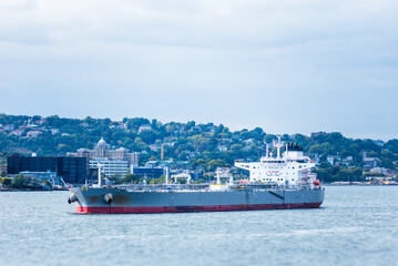 A tanker ship rests anchored in New York Bay near the shores of Mid Island, its grey painted hull...